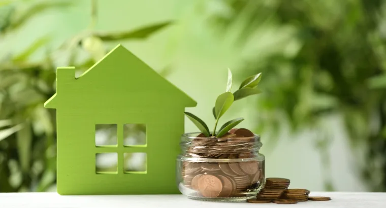 Casa verde de madera junto a un frasco de monedas con una planta que brota, símbolo del ahorro en vivienda sostenible